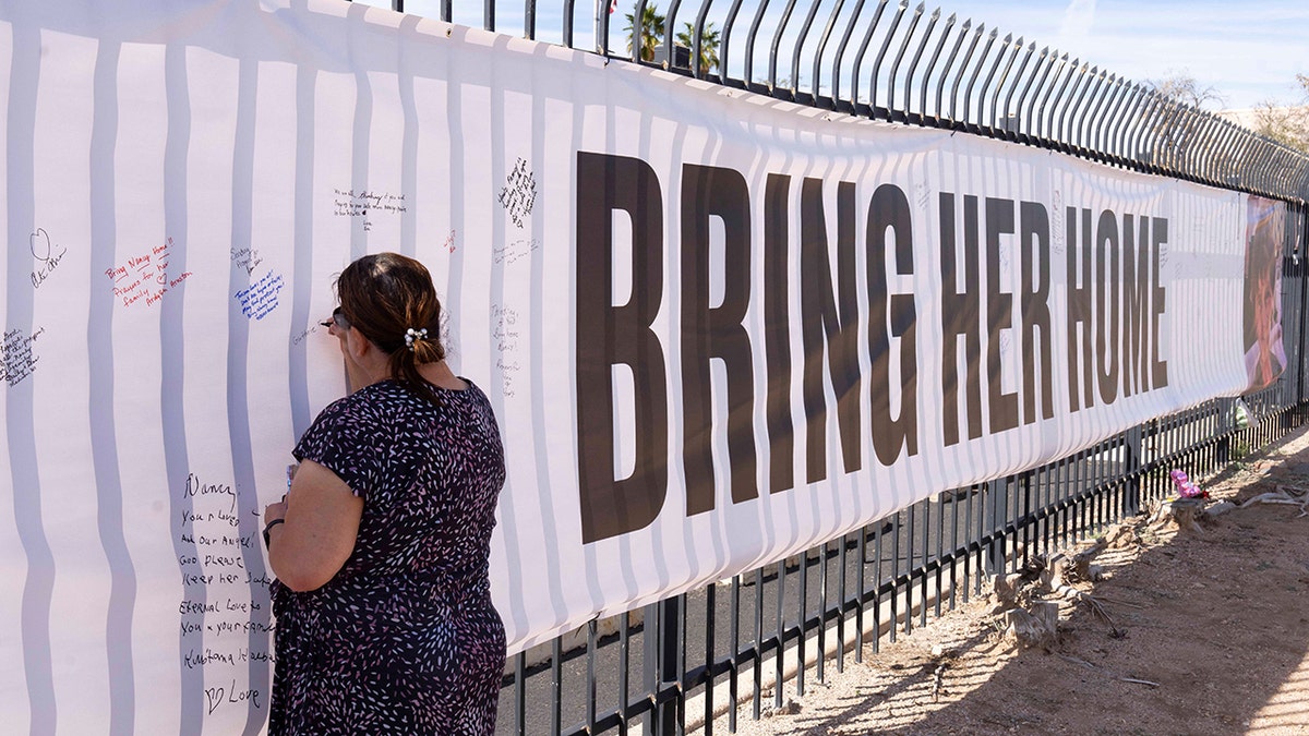 A well-wisher signing a banner featuring a photo of Nancy Guthrie and the text 