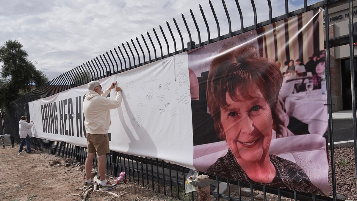 A well-wisher signing a banner featuring a photo of Nancy Guthrie and the text 
