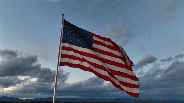 A United States flag flies over a cloudy sky.