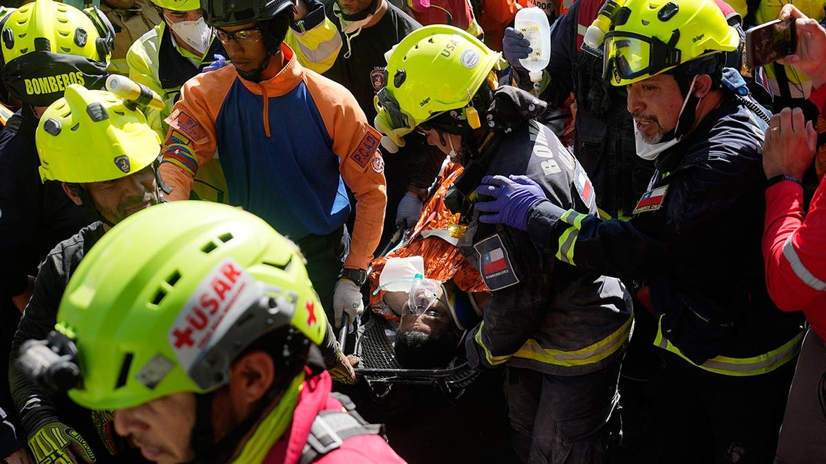 Rescuers carrying man rescued from rubble through a crowd