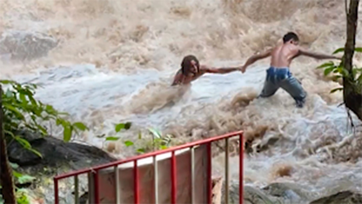 Boy pulling man from waterfall in Thailand.