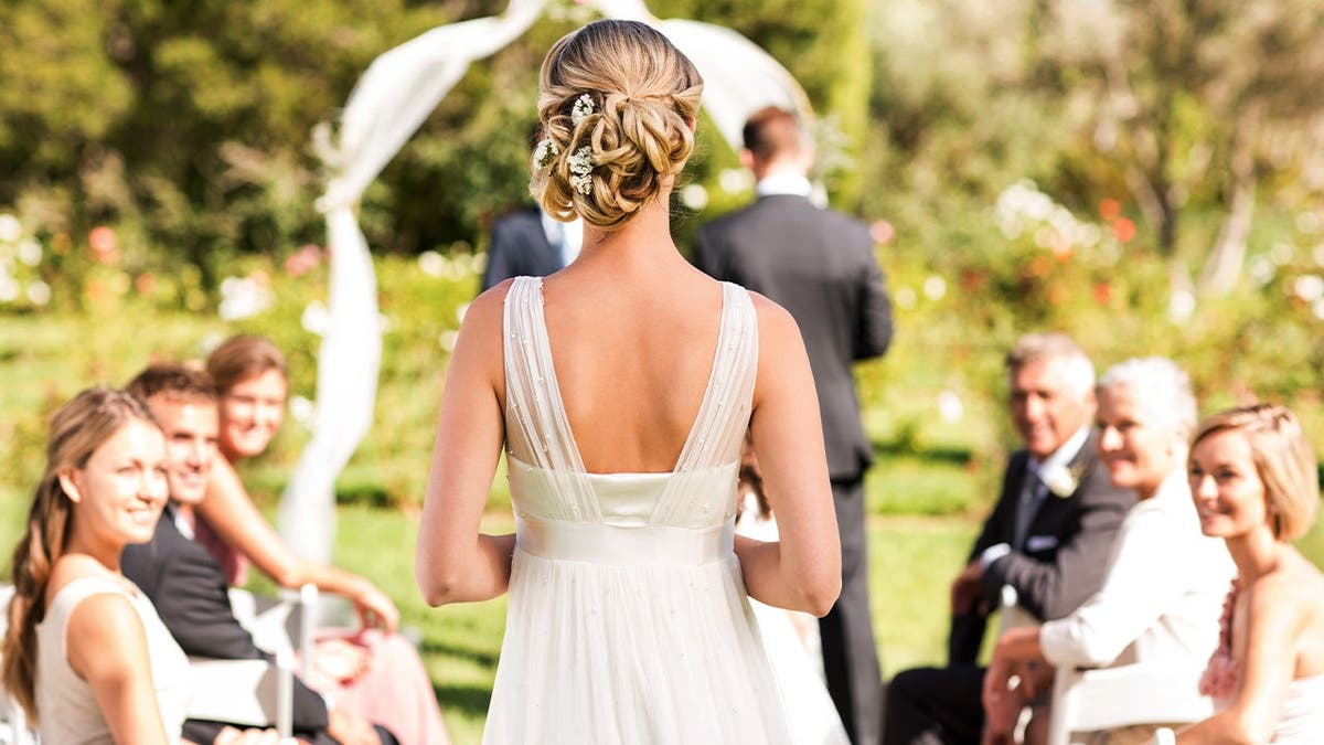 A bride walks down the aisle, wearing white.