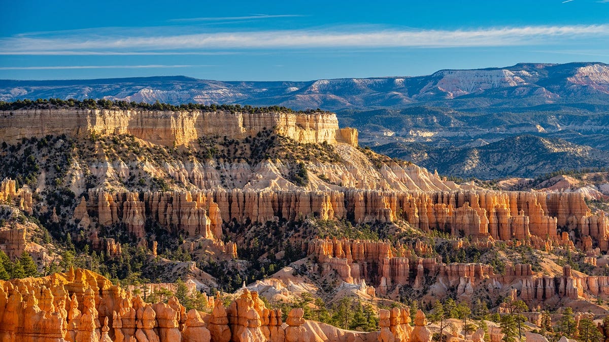 Bryce Canyon hoodoo rock formations and layered sandstone cliffs under clear blue sky at sunrise.