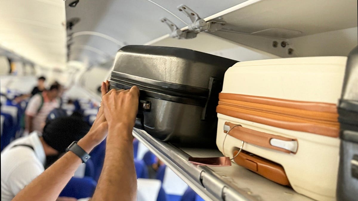 Person placing carry-on luggage in overhead compartment of airplane cabin.