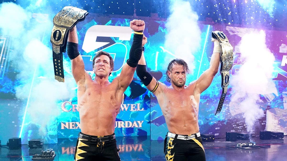 Chris Sabin and Alex Shelley hold WWE Tag Team Championship titles and celebrate in a wrestling ring.