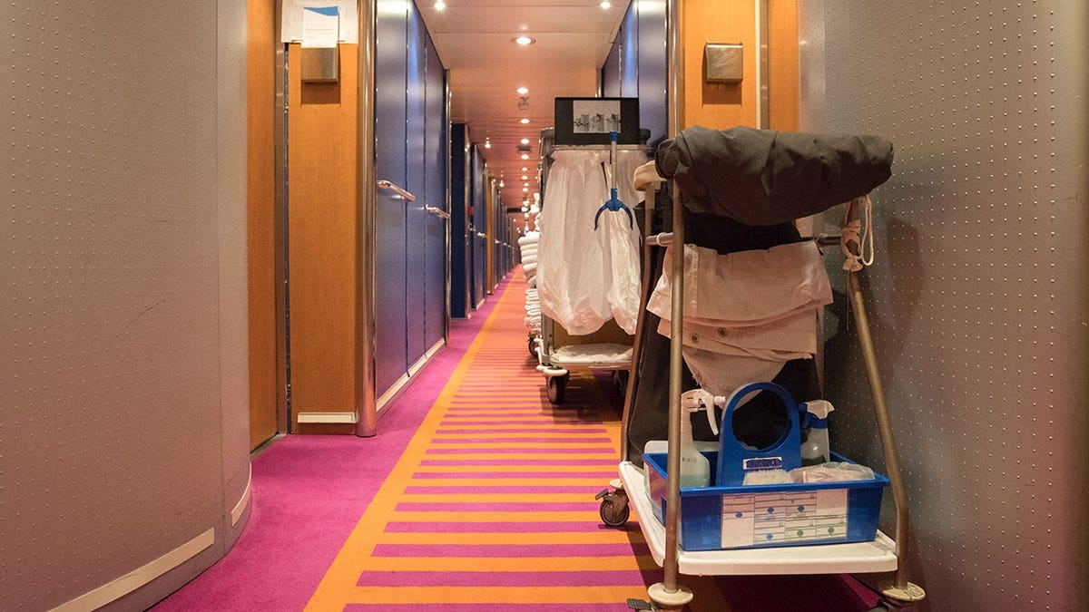 A cruise ship corridor with doors lining both sides and carpeted flooring.