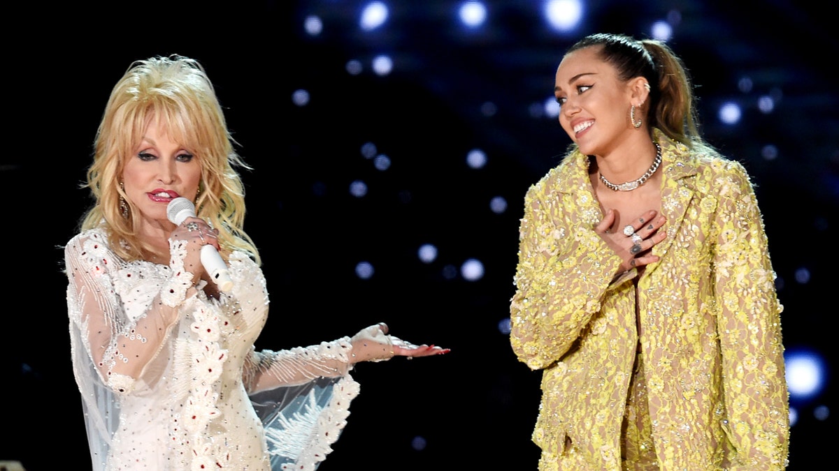 Dolly Parton and Miley Cyrus singing into microphones while performing on a stage.