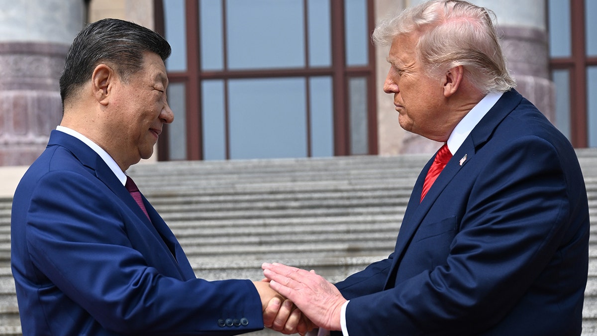 Xi Jinping and Donald Trump shake hands while looking at each other in front of stone steps.