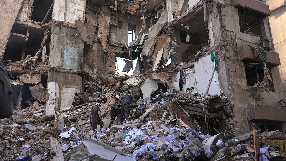 Lebanese civil defense workers search through the concrete rubble and twisted metal of a destroyed building.
