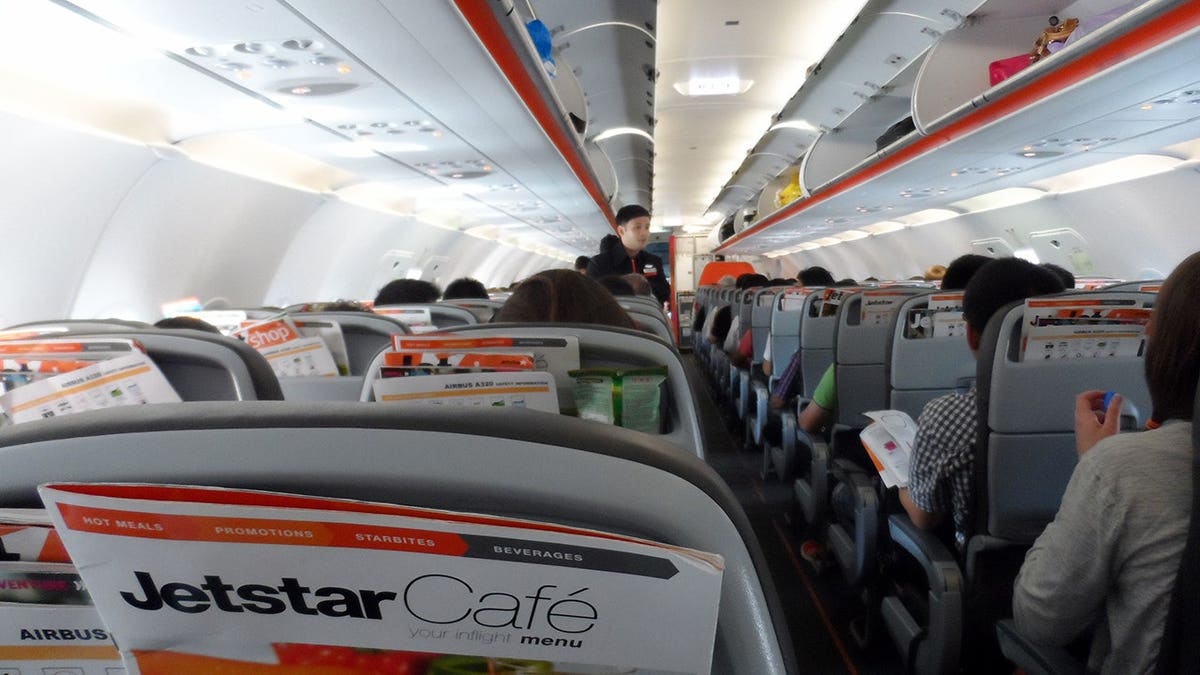Jetstar Airways cabin interior with passenger seats, flight attendant and passengers.