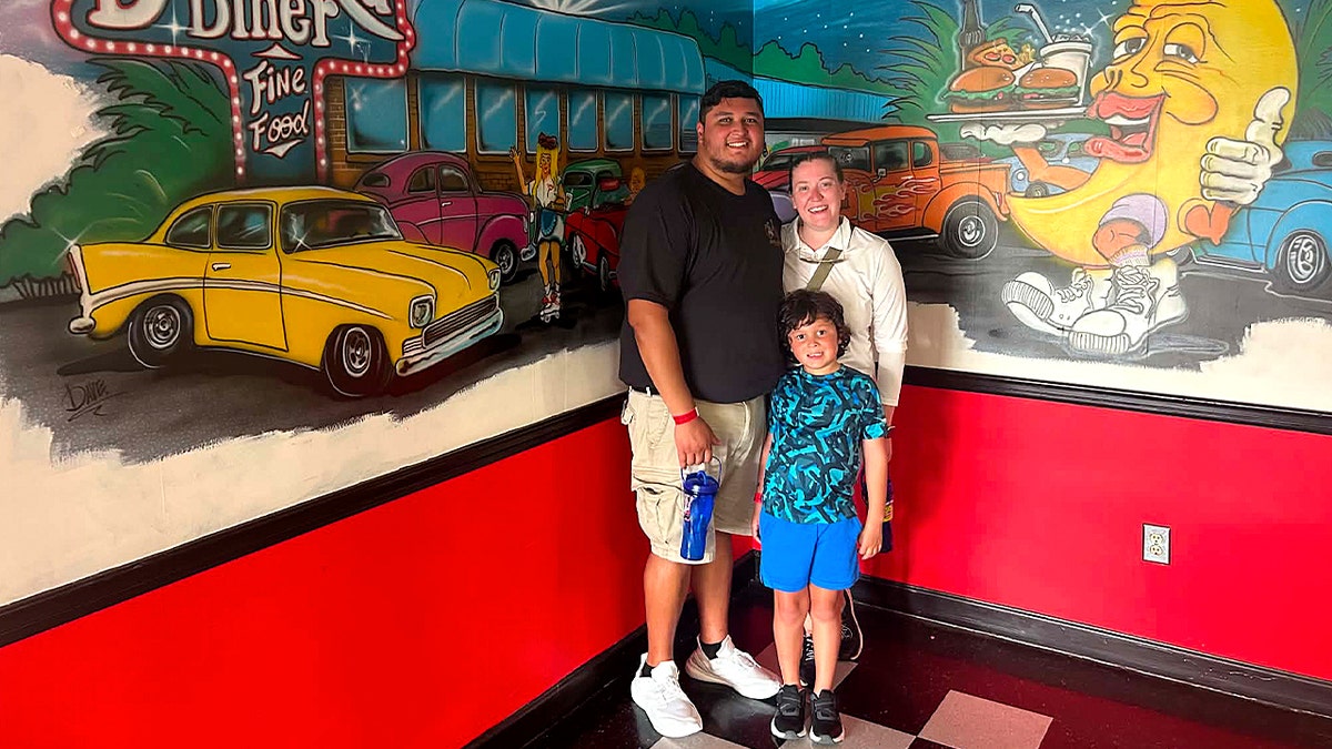 a young boy with curly hair standing with his parents inside a diner