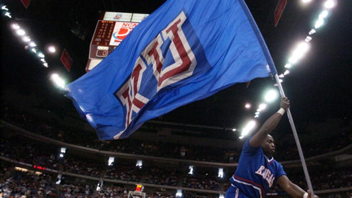 Kansas cheerleader waves school flag as team enters court before NCAA tournament game.