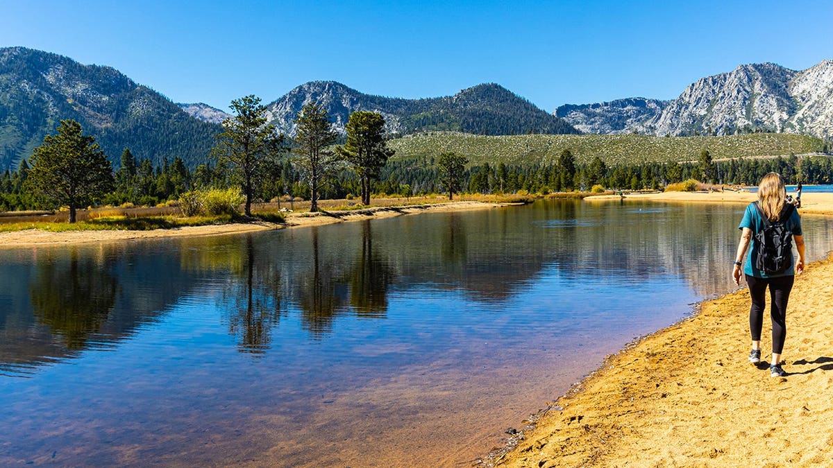 Female hiker walks on sandy shore at Kiva Beach, Lake Tahoe.