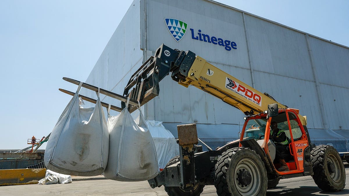 A forklift carries bags of waste in front of Lineage Logistics building.