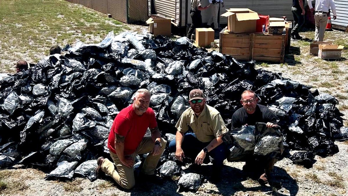 Officials standing near a mountain of suspected black market marijuana in plastic bags
