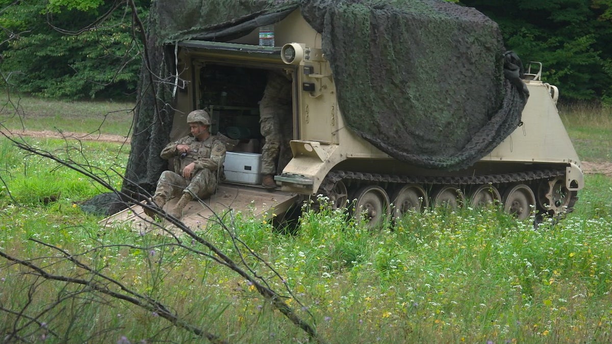 Soldier rests beside a military vehicle during Northern Strike training in Michigan.