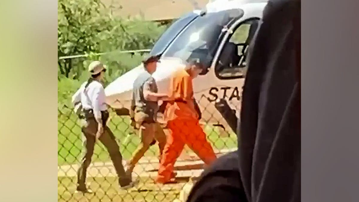 Federal police usher the neck-slashing suspect off to the helicopter