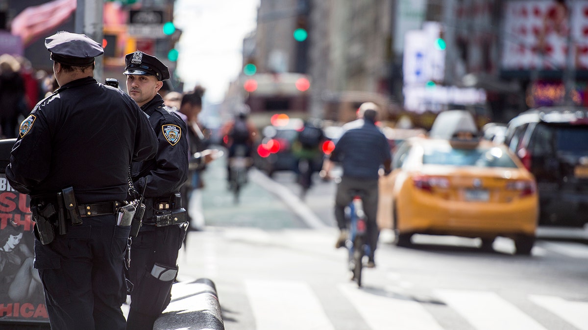 Shot of Times Square in NYC at bicyclists and taxis pass and two police officers stand off to the side.