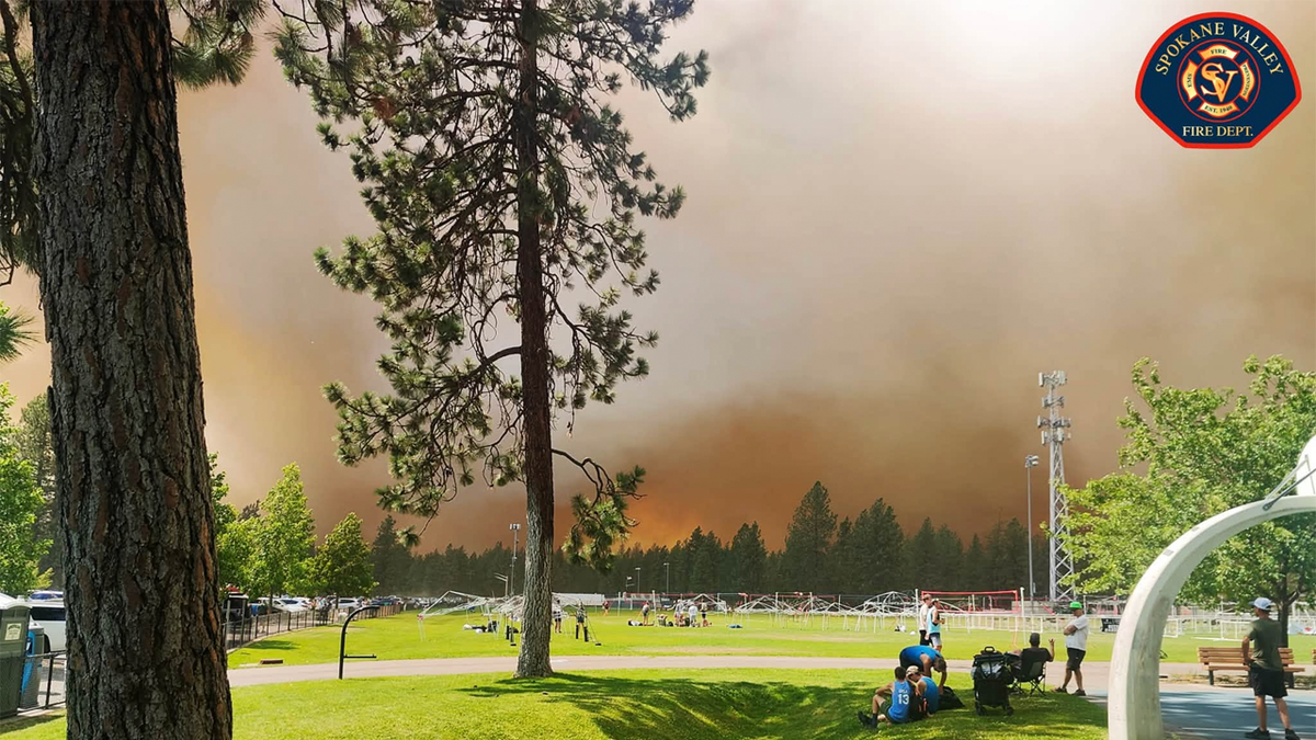 Towering smoke from a fast-moving wildfire rises behind a park in the Spokane area as firefighters battle multiple blazes