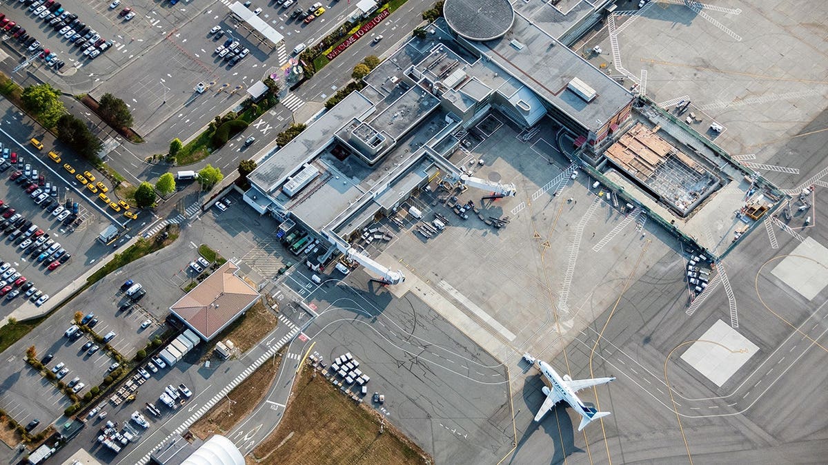 Aircraft is guided to a terminal at Victoria International Airport as vehicles sit parked nearby.