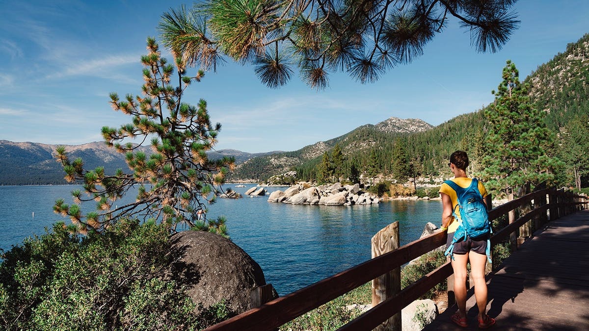 Woman stands at Lake Tahoe with snow-covered Sierra Nevada mountains in the background.