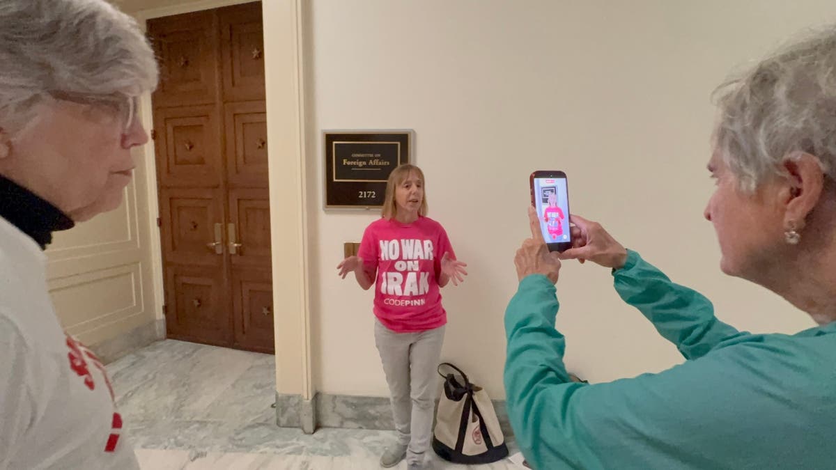 On Sept. 15, 2026, CodePink co-founder Medea Benjamin poses outside the House Foreign Affairs Committee hearing room, a Trader's Joe bag beside her feet.