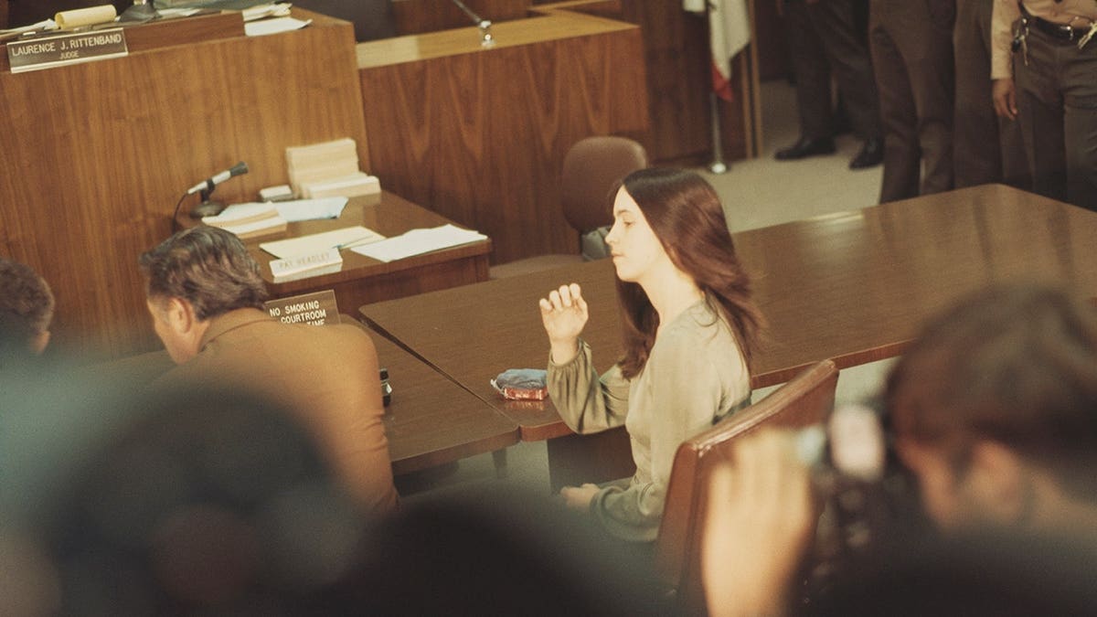 Susan Atkins sits at the defendant's table in a courthouse.