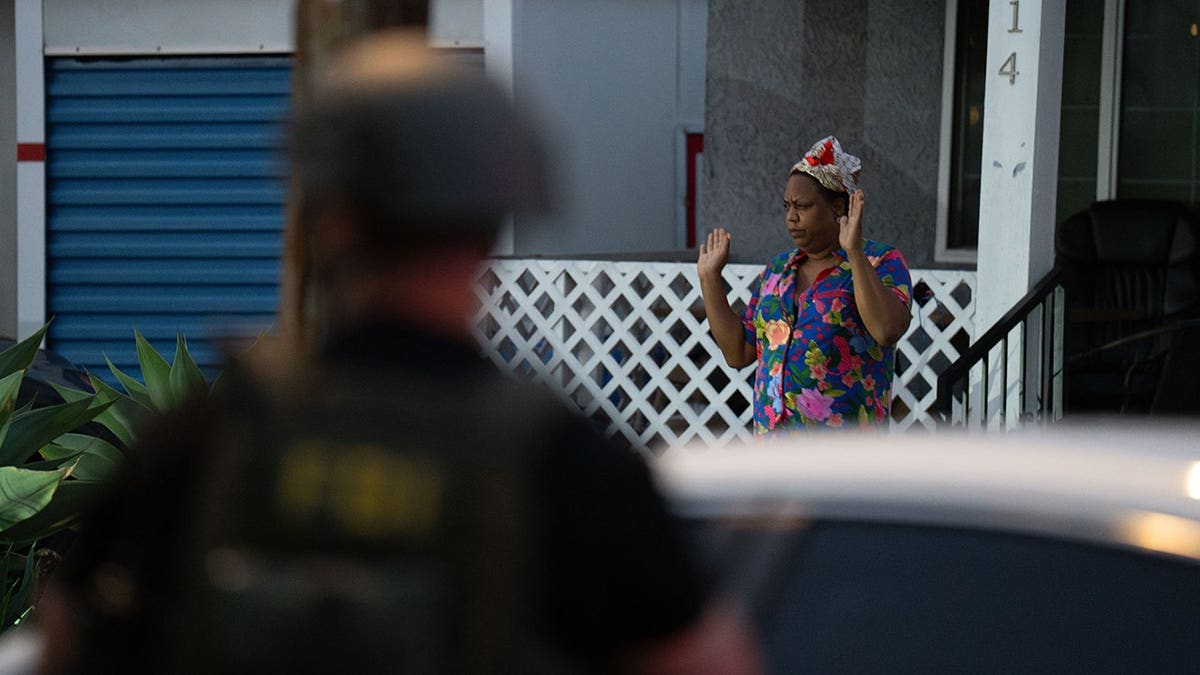 Lakiya Malone walks out of her home with her hand raised toward federal authorities in Los Angeles.