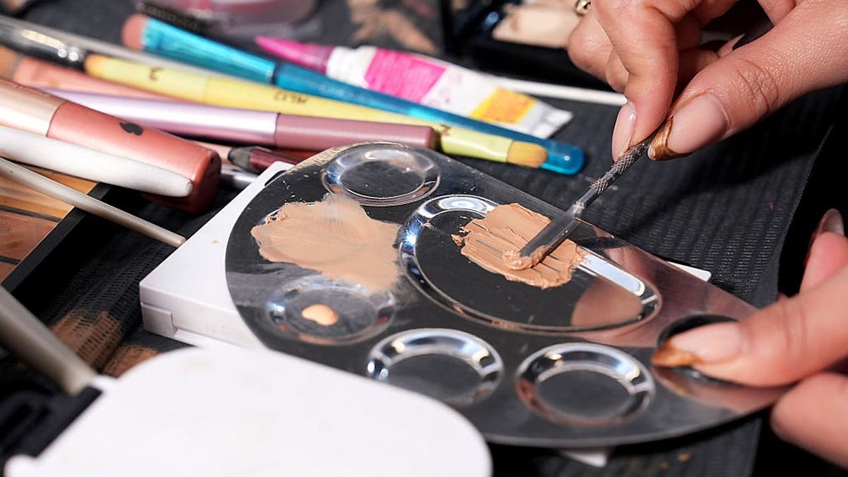 Makeup artist mixes concealer on a palette during a fashion show.