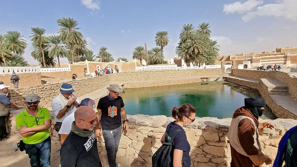 European tourists walk past a spring water pool in Ghadames with security personnel nearby.