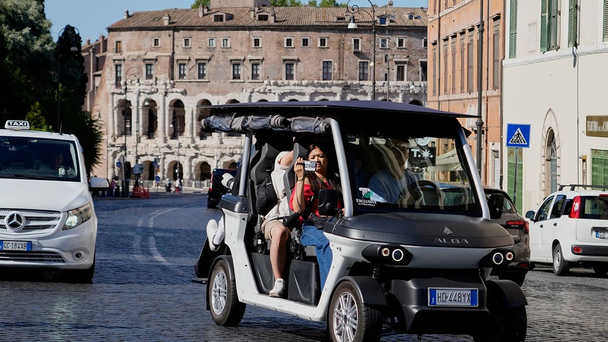 Tourists ride in a golf cart traveling through central Rome.