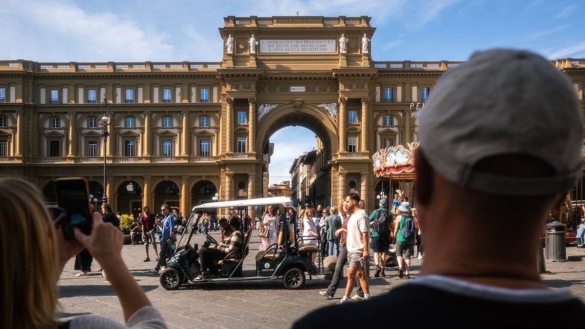 Two tourists photograph a golf cart parked in Piazza della Repubblica, Florence.