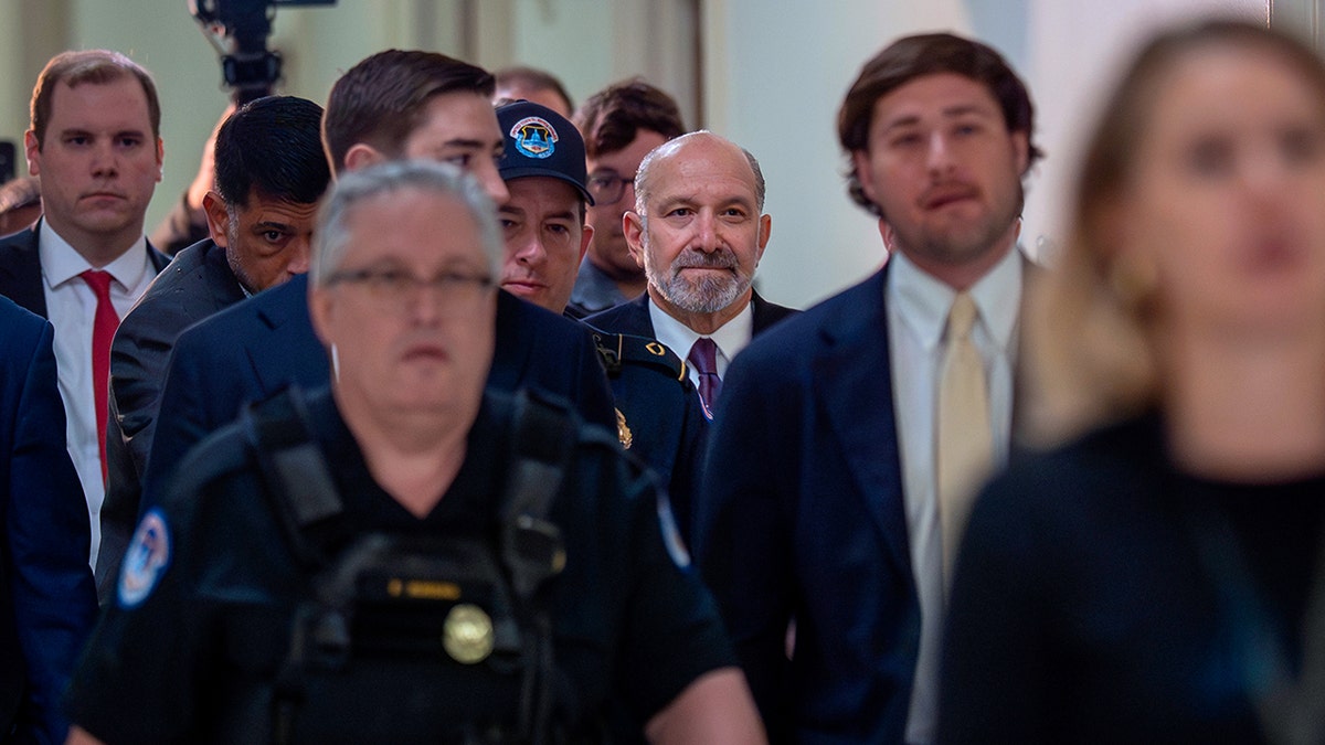 Howard Lutnick walks through a crowded hallway in the U.S. Capitol while surrounded by security and staff.