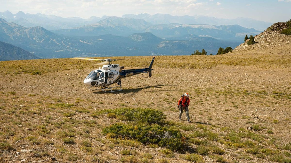 A man getting off a helicopter to rescue a climber on a mountain.