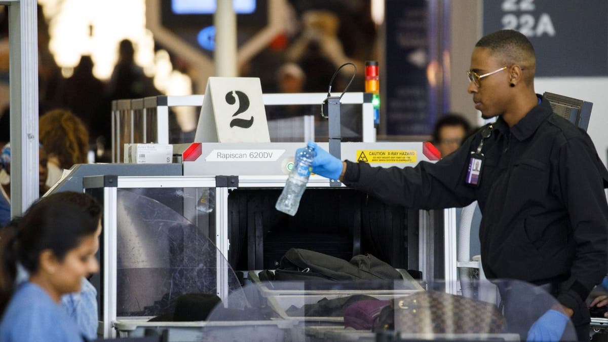 An agent removes a water bottle as baggage is screened at a Transportation Security Administration (TSA) checkpoint